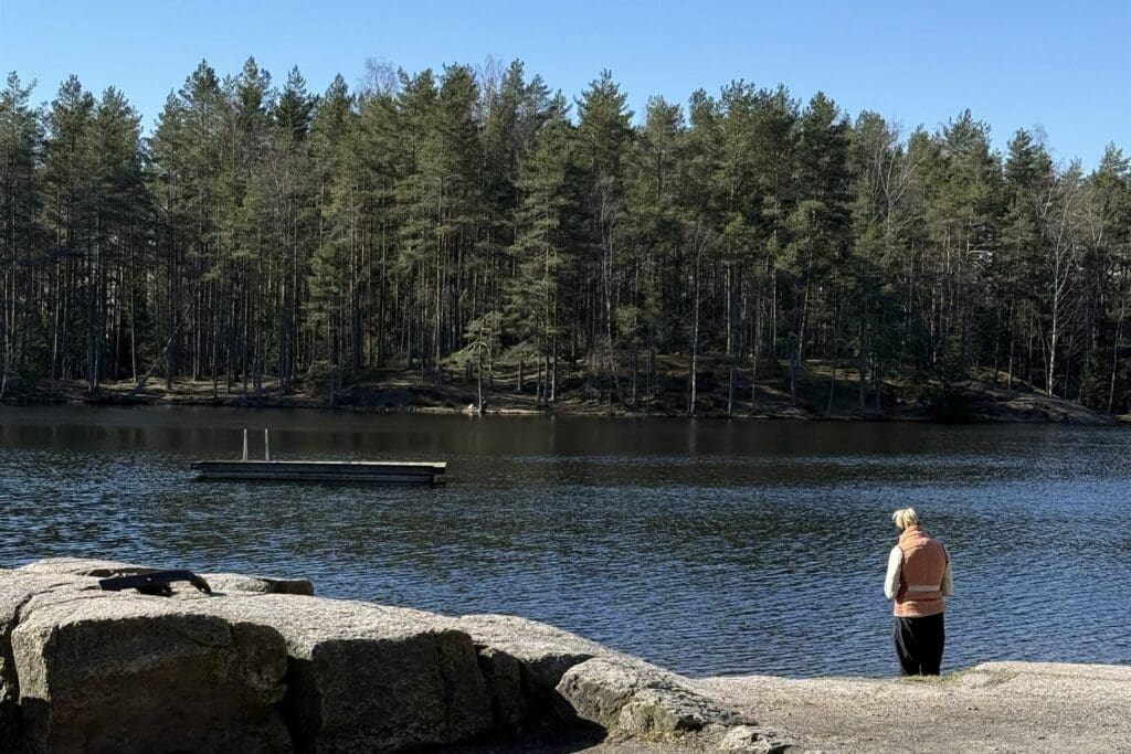 Person står ved et skogsvann med flytebrygge en solrik dag